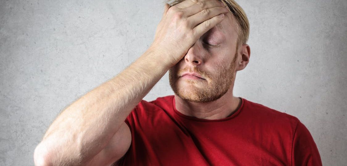 Man wearing a red shirt holding his forehead