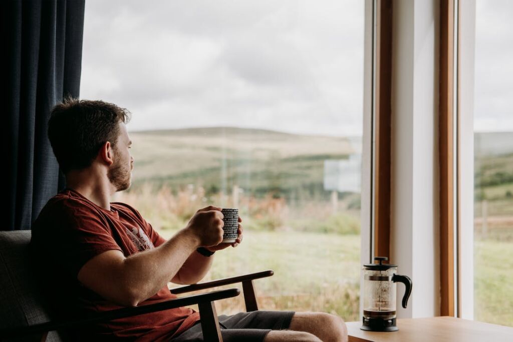 Man sitting in a porch looking over a field while drinking coffee