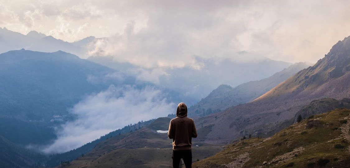 Person wearing a hoodie standing atop a mountain