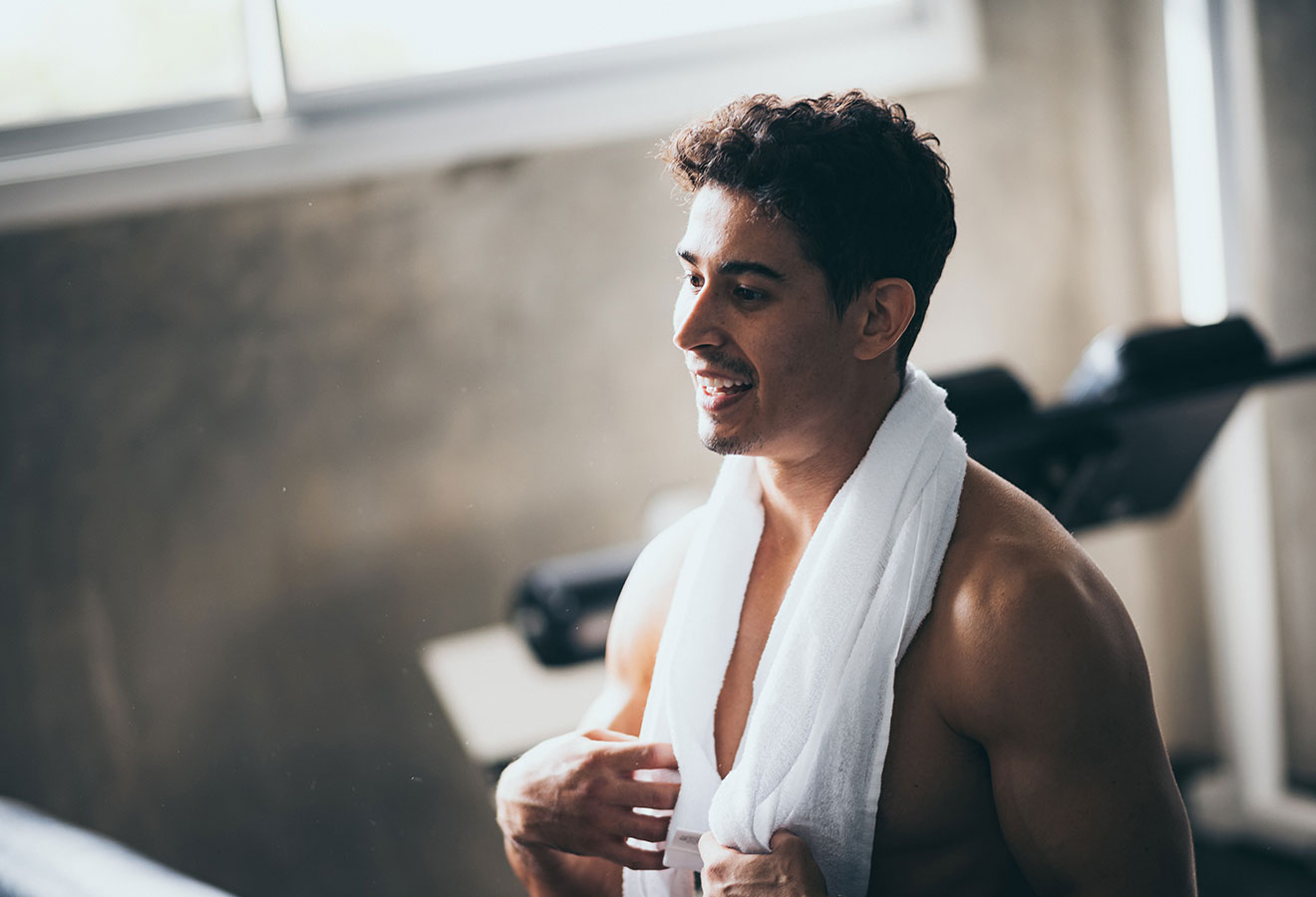 Man standing in a gym with a towel around his neck and no shirt on
