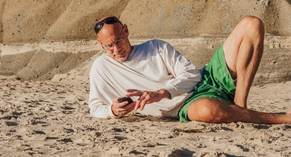 Older man laying on the beach while on his phone